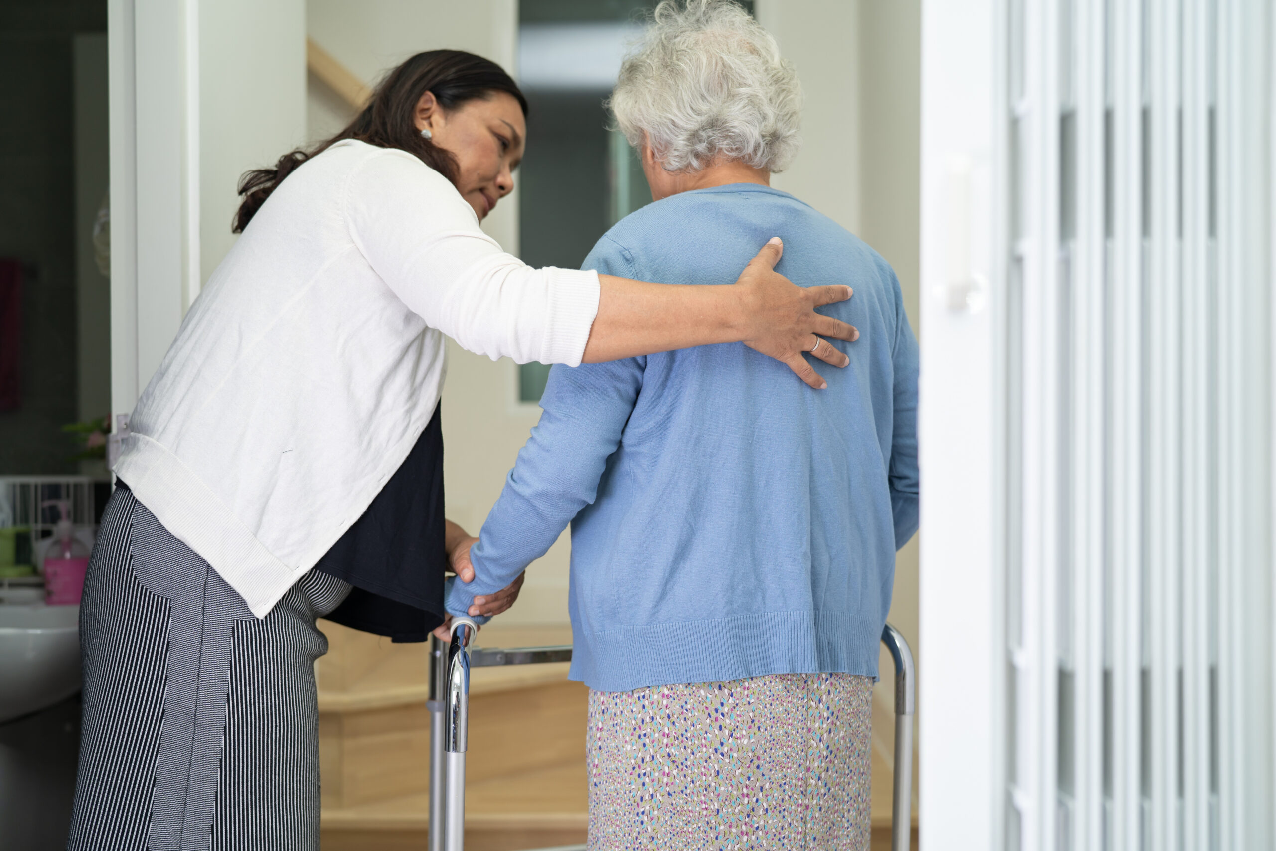 Caregiver help asian or elderly old woman walk with walker support up the stairs in home.